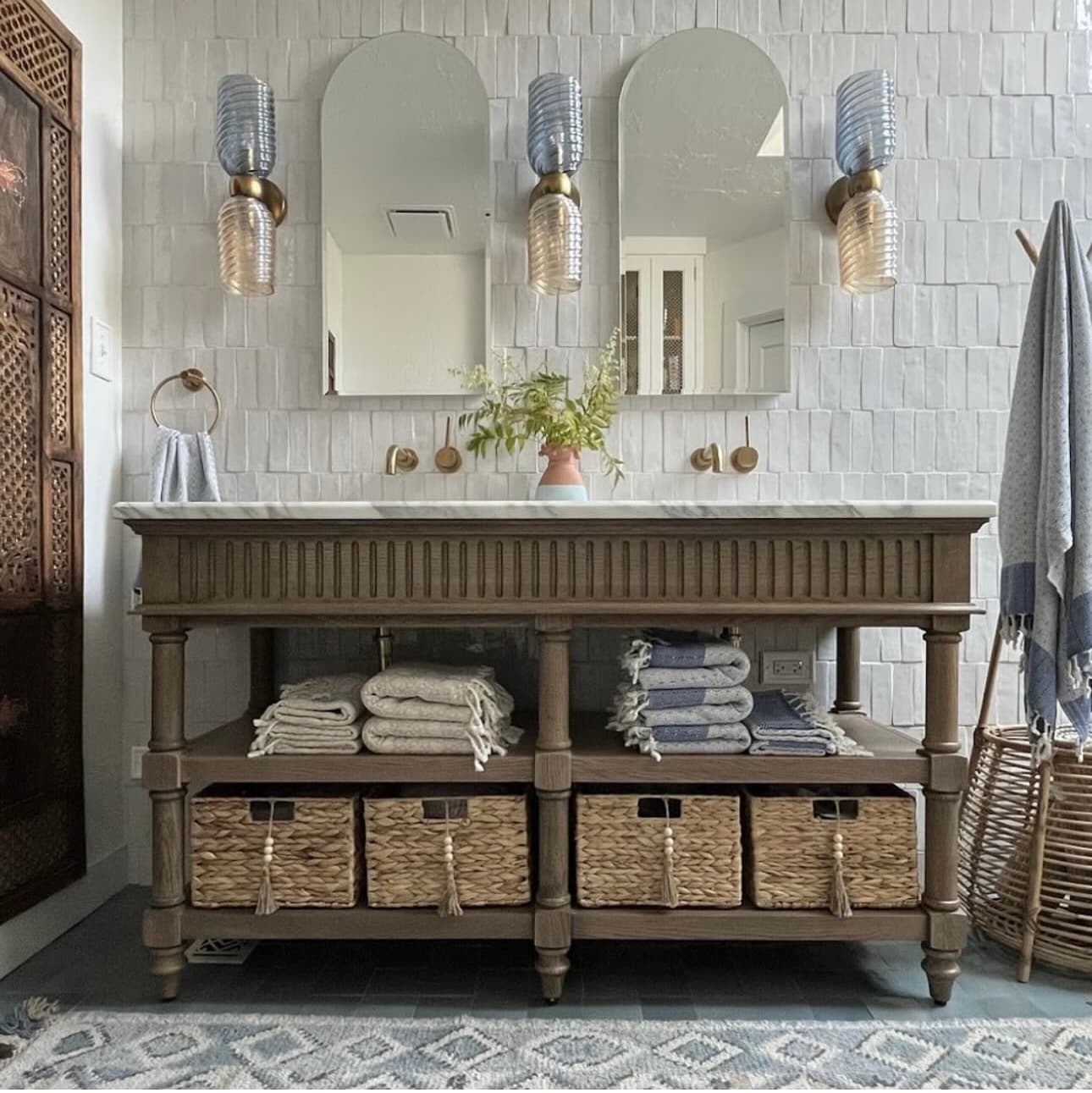 Double vanity with a white marble top, brass wall-mounted faucets, arched mirrors and glass sconces